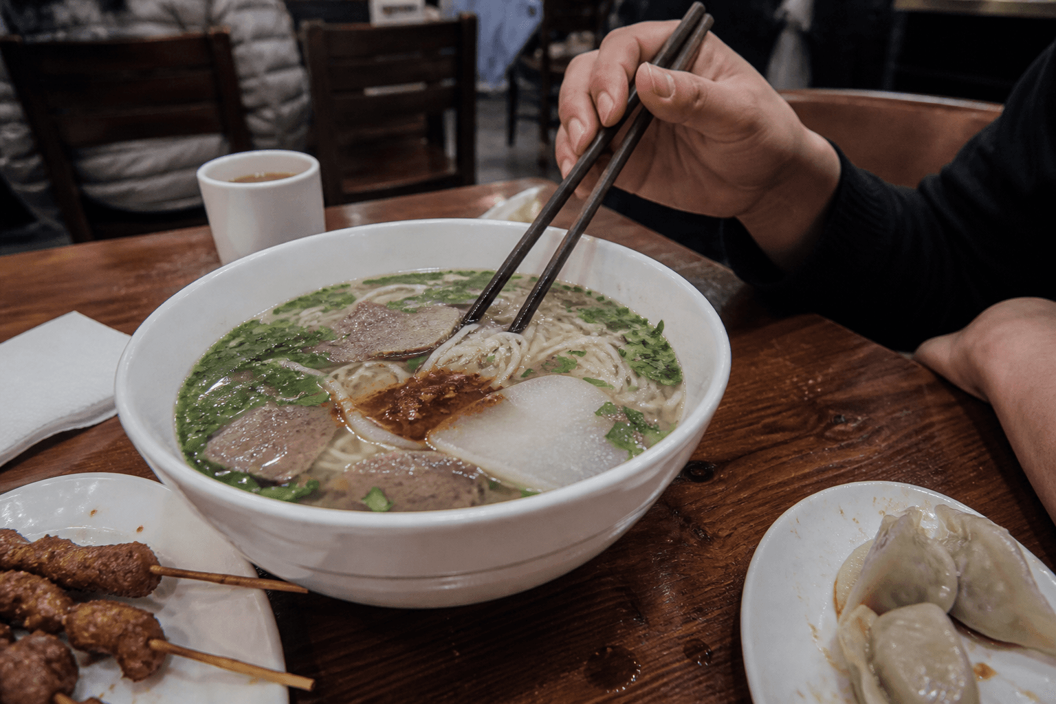 A Chinese halal meal with clear-broth beef noodles, lamb skewers, and beef dumplings