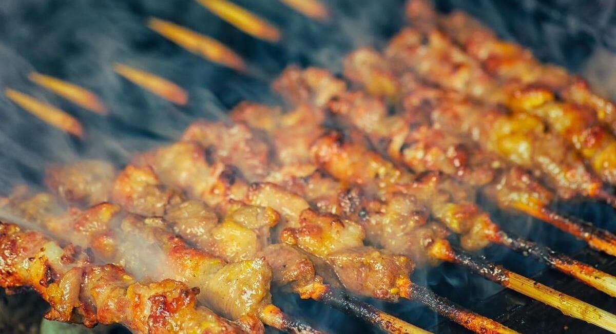 Charcoal-grilled lamb skewers dusted with cumin and chilli, smoke rising